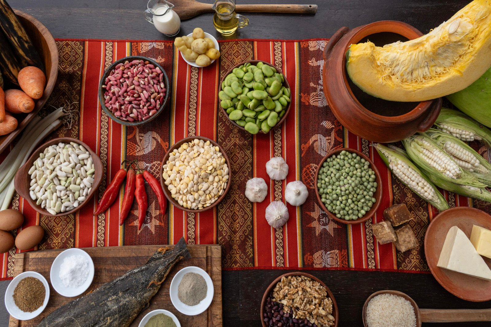 Ingredientes de la fanesca tradicional ecuatoriana organizados sobre una mesa con granos, choclo, zapallo, bacalao, especias y productos frescos.