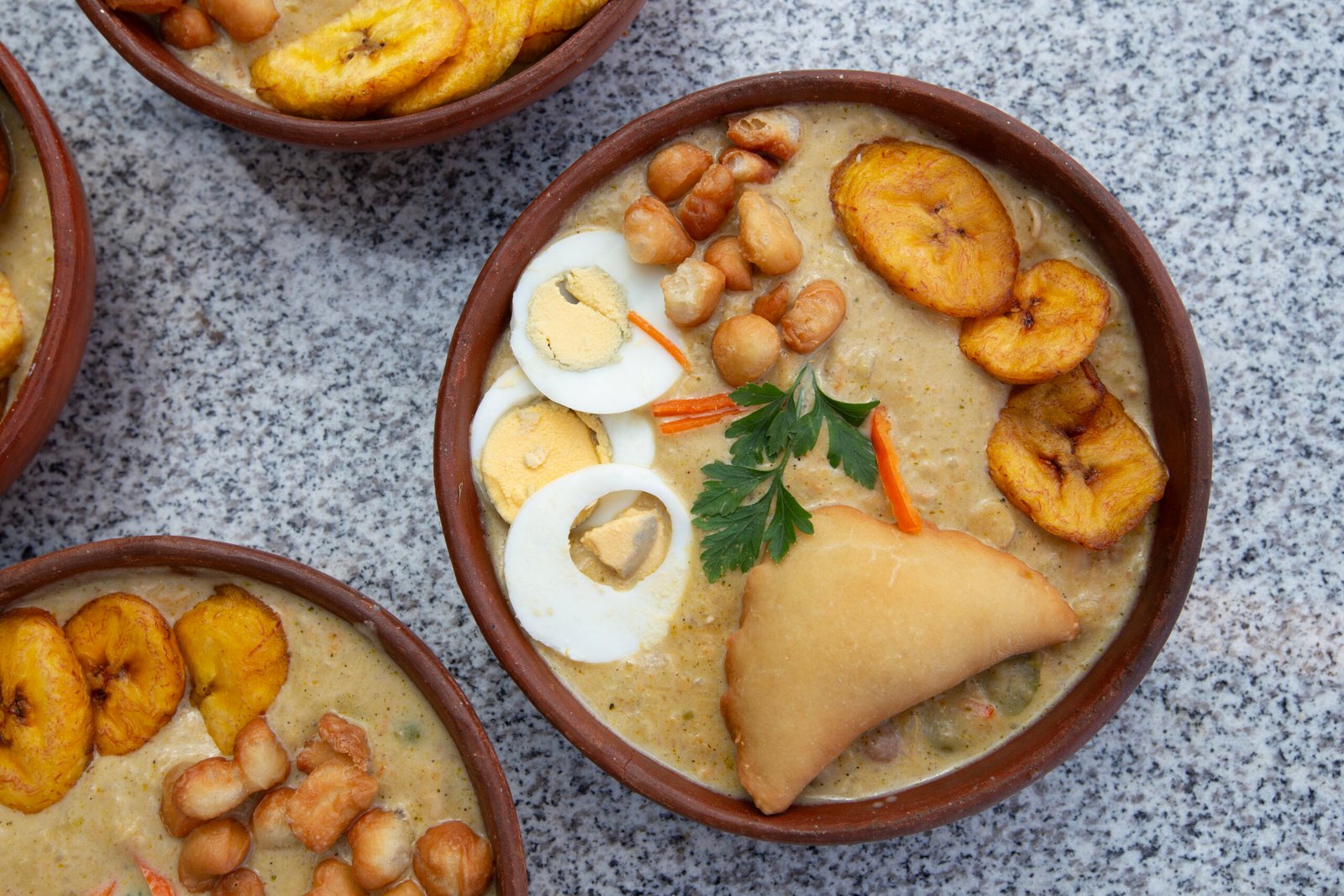 Platos de fanesca decorados con sus acompañantes, huevo, fritos, empanada, aji. Listos para servir y degustar.